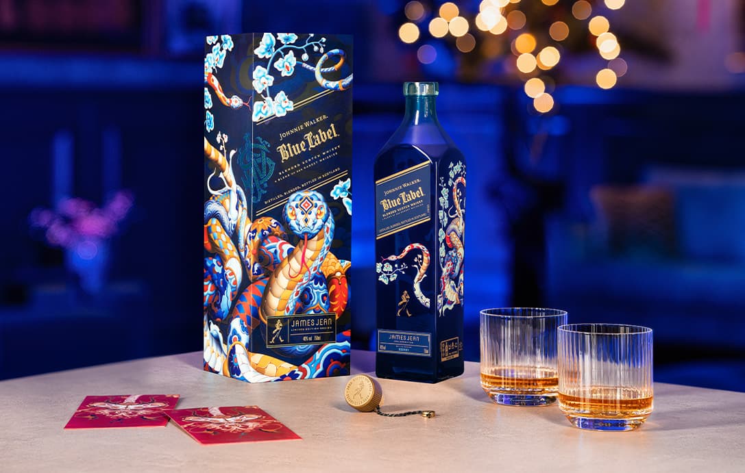 A bottle of Johnnie Walker Lunar New Year 2025 on a table with two glasses of whiskies and two red cards