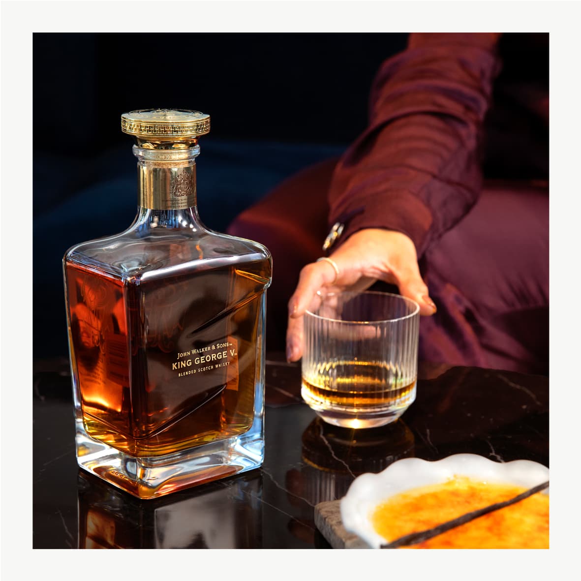 John Walker & Sons King George V Blended Scotch Whisky bottle and a person holding a glass of whiskey